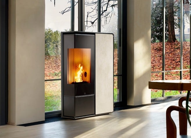 Cheminée moderne à granulés noire avec flamme visible et panneau clair devant une grande baie vitrée donnant sur un paysage d'automne.