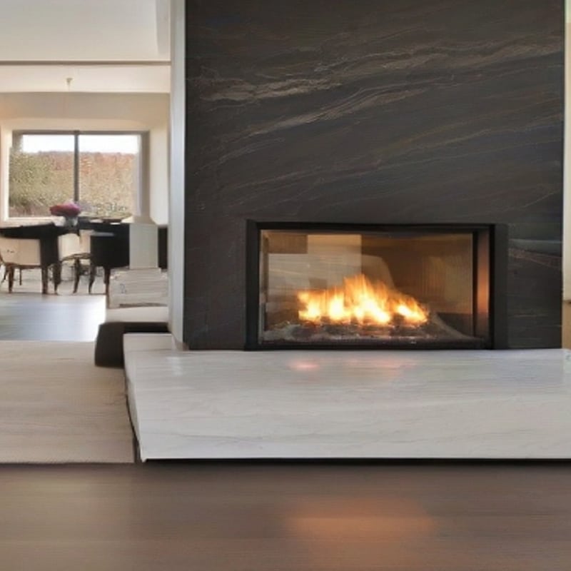 Cheminée moderne encastrée à foyer vitré et flammes vives. Revêtement en pierre sombre texturée, âtre blanc. Vue sur intérieur lumineux.