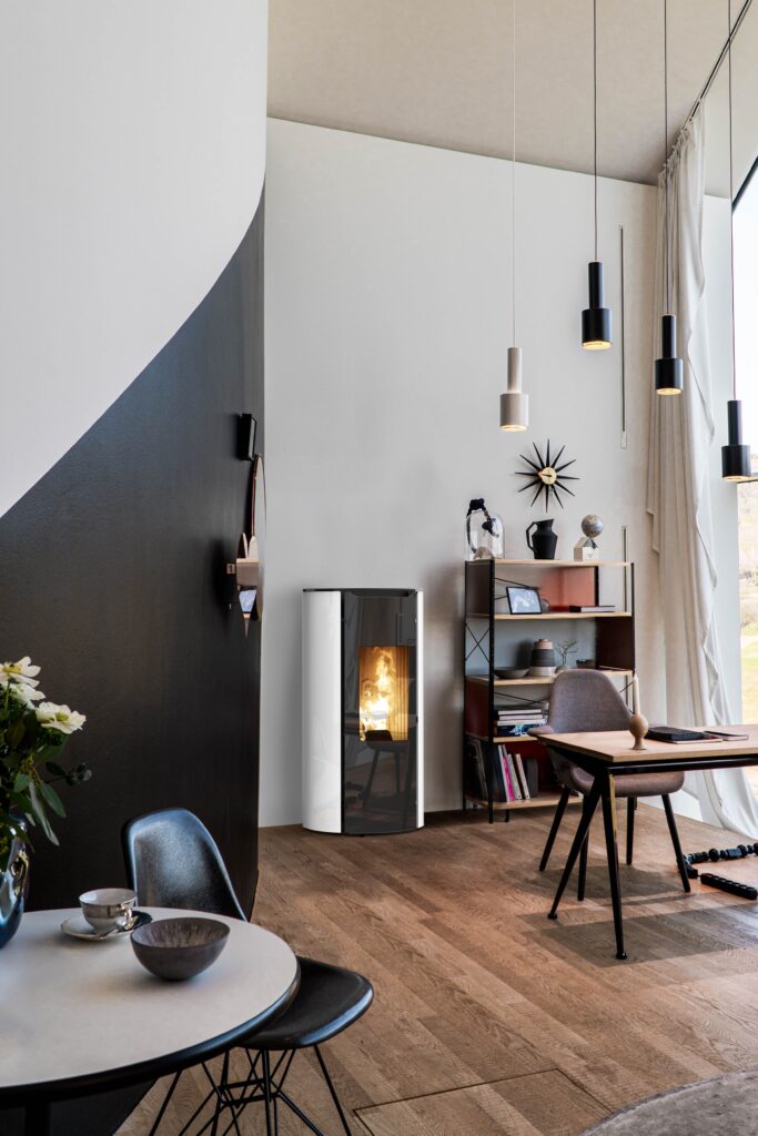 Intérieur moderne lumineux avec poêle à granulés blanc et flamme, plancher bois clair. Mur bicolore noir/blanc, coin repas et bureau design.